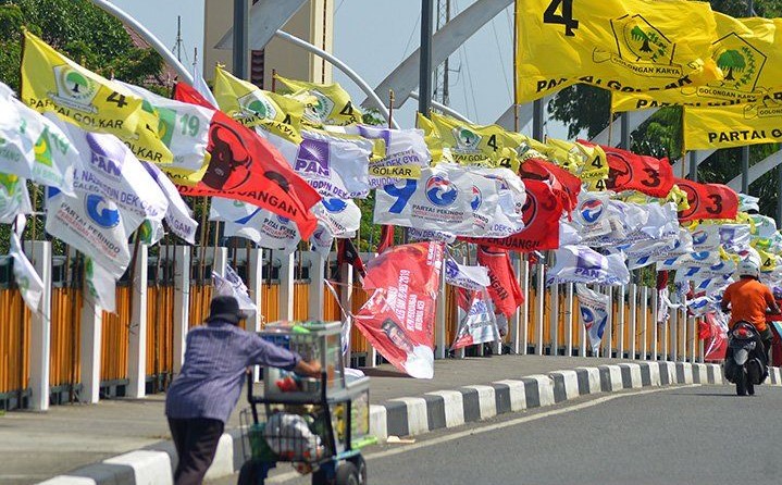 Ilustrasi-masyarakat melintas di jalan yang dipenuhi bendera partai peserta pemilu. (foto:gemapos/ant)